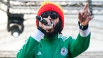 Protoje mit Mütze und Trainingsjacke zeigt ins Publikum und singt