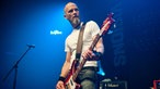 Der Bassist der Band vor dem blau leuchtenden Rockpalast Schild.