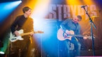 Pete MacLeod mit Akustik-Gitarre im Jeans-Outfit neben Andy Conner mit E-Gitarre in Schwarz.