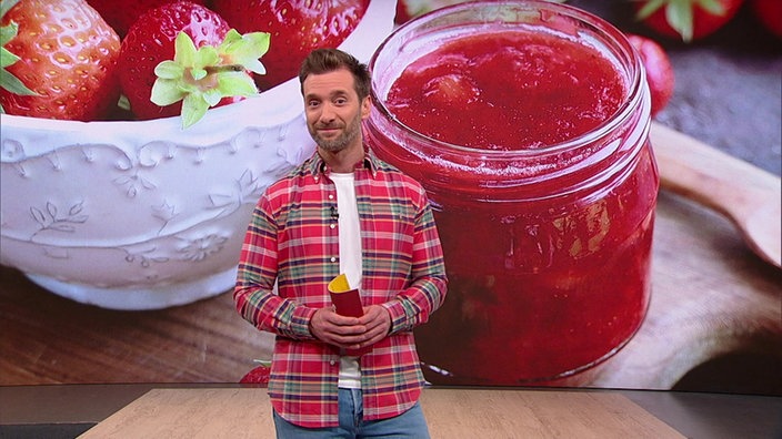 Das Bild zeigt Daniel Aßmann im Servicezeit-Fernsehstudio. Im Hintergrund ist ein Glas mit Konfitüre zu sehen.