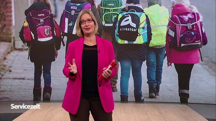 Die Moderatorin im Studio vor der Bild einer Gruppe Kinder auf dem Weg zur Schule