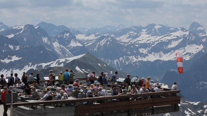 Außengastronomie auf Aussichtsplattform vor schneebedeckten Bergen