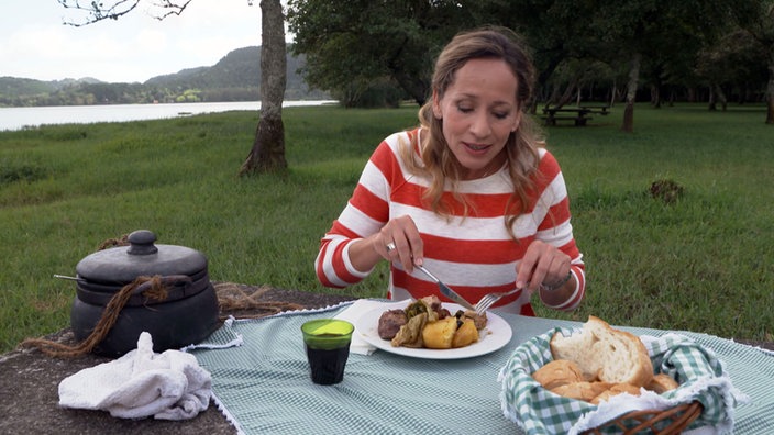 Tamina Kallert sitzt in freier Natur an einem Tisch und isst ein Eintopfgericht