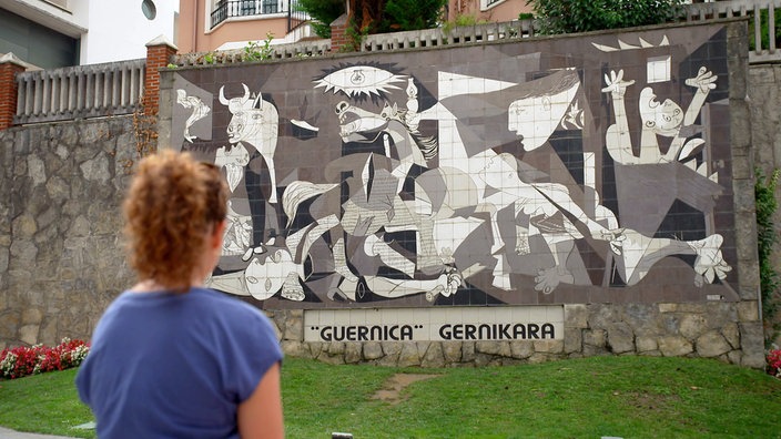 Anne Willmes steht vor einer Wand mit der Abbildung des Gemäldes Guernica