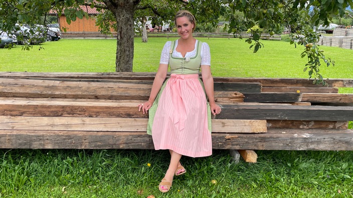 Judith Rakers im Dirndl sitzend auf einem Holzstapel