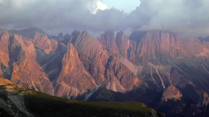 Felsmassiv mit mehreren Bergspitzen erscheint rötlich im Licht des Sonnenuntergangs