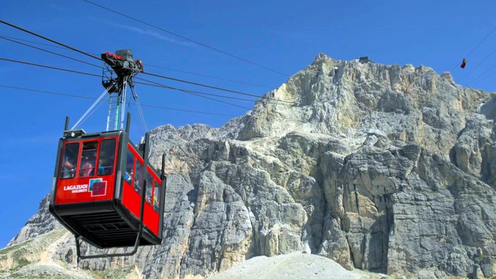 Rote Seilbahngondel auf dem Weg zu einem felsigen Bergmassiv