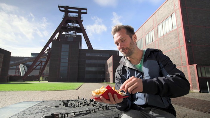 Daniel Aßmann isst Pommes, im Hintergrund der Förderturm der Zeche Zollverein 