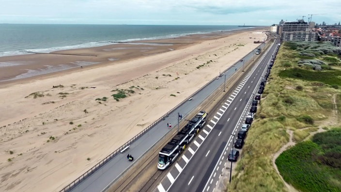 Blick von oben auf die Straßenbahnstrecke mit Bahn entlang eines sehr langen Sandstrandes