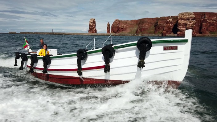 Anne Willmes mit Kapitän Sven Köhn in einem Börteboot auf See, im Hintergrund die roten Felsen von Helgoland