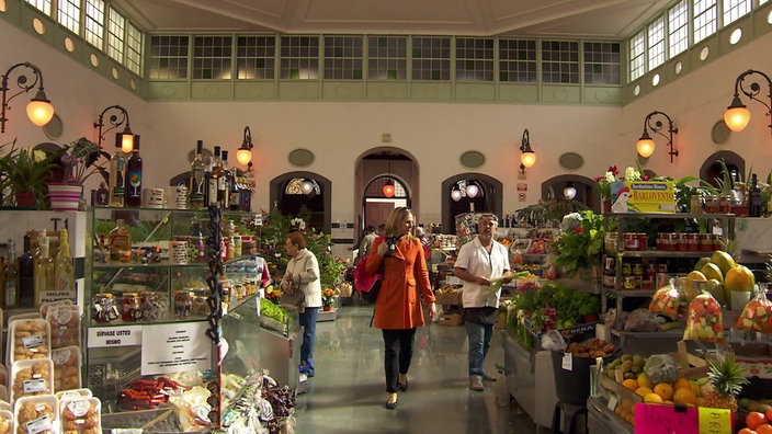  Andrea Grießmann in einer Markthalle mit vielen Obst- und Gemüseständen