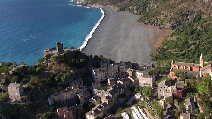 Blick von oben auf das mittelalterliche Bergdorf Nonza, weiter unterhalb Bucht mit grau-grünem Strand. 