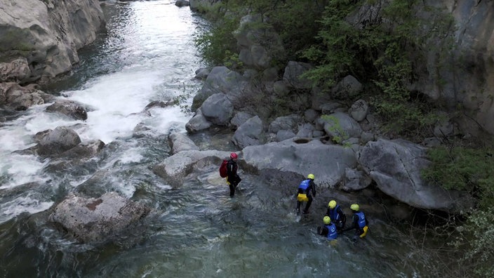 Eine Gruppe in Schutzanzügen und mit Helmen betreibt Canyoning in einem Wildwasserfluss