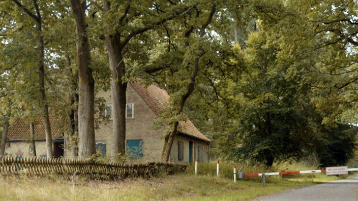 Verlassenes Haus unter Bäumen, daneben eine geschlossene Straßenschranke