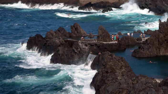 Brandung an dunklen Felsen, in denen sich kleine Pools befinden