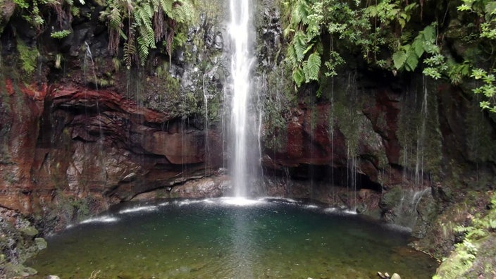 Wasserfall stürzt vor Felsenwand in einen blaugrünen See