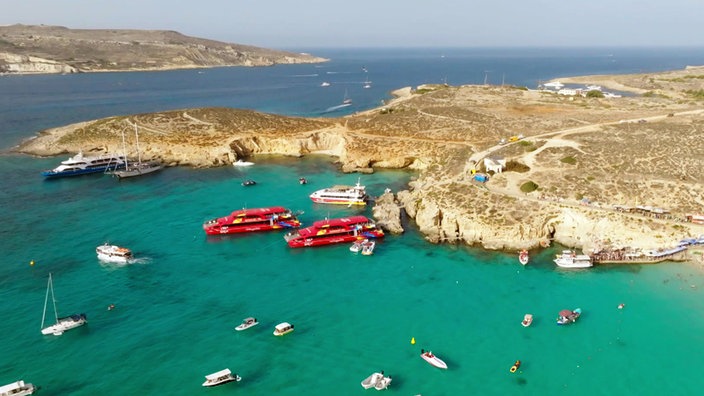 Blick von oben auf Bucht mit türkisfarbenem Wasser und mehreren Booten