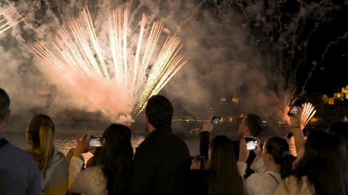 Mehrere Personen schauen einem Feuerwerk über der Stadt zu