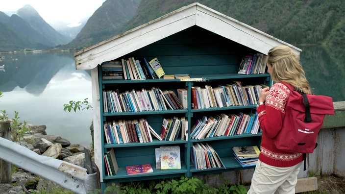 Tamina Kallert steht vor einem öffentlichen Bücherregal im Bücherdorf Fjaerland.