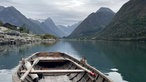 Blick über ein altes Ruderboot auf Gewässer und schneebedeckte Berggipfel