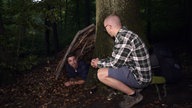 Ramon Babazadeh liegt in einer selbst gebauten Laubhütte im Wald 