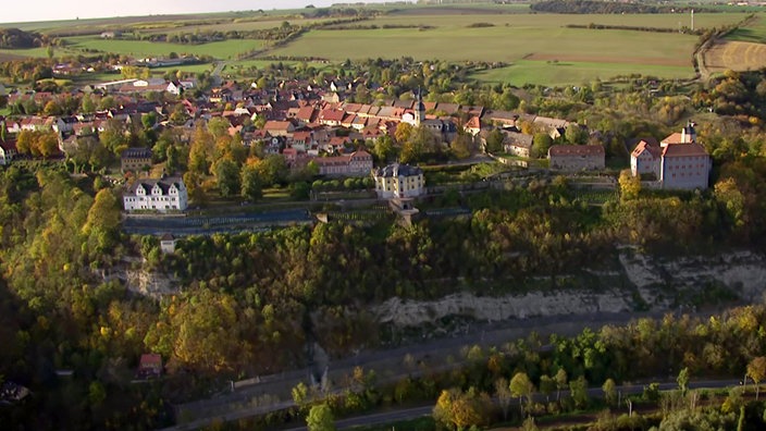 Drei nebeneinanderliegende Schlösser am Rande eines Felshangs, dahinter ein Dorf