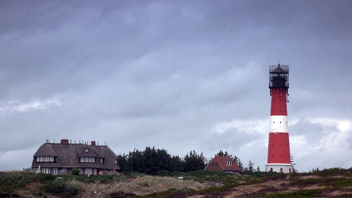 Rot-weißer Leuchtturm neben reetgedecktem Haus