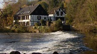 Blick über einen Fluss auf ein Fachwerkhaus mit Nebengebäude