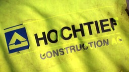 Der Schriftzug "Hochtief" blättert von einer Regenjacke ab