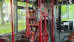 In einem Linienbus steht hinter dem Fahrersitz ein Regal mit Büchern