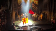 Ein Klimaaktivist hält auf einer Theaterbühne eine Flagge mit einem stilisierten Totenkopf.