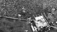 Schwarzweißaufnahme vom 16.08.1969: Die Bühne des Woodstock-Festivals und Tausende Fans, Blick aus der Vogelperspektive