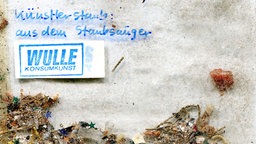 Ein Beutel mit Staub und der Beschriftung "Künstlerstaub aus dem Staubsauger - WULLE KONSUMKUNST".