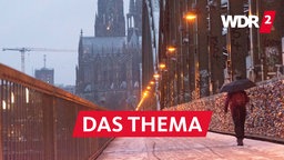 Eine Person mit Schirm spaziert über die Hollenzollernbrücke in Köln auf den Dom zu