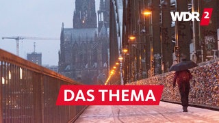 Eine Person mit Schirm spaziert über die Hollenzollernbrücke in Köln auf den Dom zu