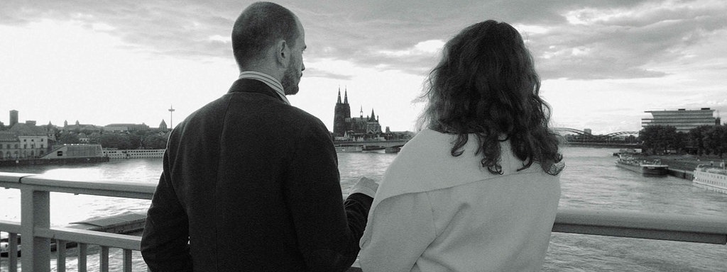 Ein Pärchen steht nach Norden schauend auf der Sevrinsbrücke in Köln, von hinten fotografiert, schwarzweiß.