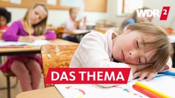 Ein Mädchen sitzt in einem Klassenzimmer, hat die Augen geschlossen und den Kopf auf den Tisch gelegt