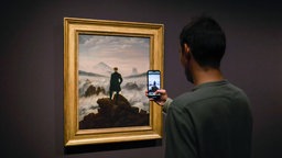 Eien Person fotografiert das Gemälde "Wanderer über dem Nebelmeer" von Caspar David Friedrich.