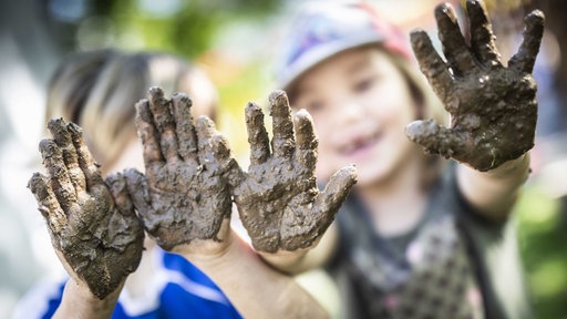 wei Kinder zeigen ihre Matschhände im Garten der "Freien Kinderschule" im Stadtteil Unterliederbach. Die Einrichtung existiert seit über 40 Jahren. Angefangen hat alles 1969 in Schwalbach, als Eltern einen der ersten Kinderläden gründeten.