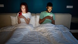 Junges Paar, das abends zusammen im Bett liegt und Smartphones benutzt.