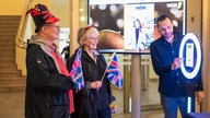 Zwei Konzertbegeisterte in Verkleidung mit Union Jack Fähnchen vor einem Fotoautomat.