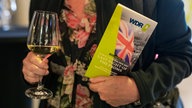 Ein Mensch mit einem Sektglas und dem Programm Flyer der WDR 3 "BBC Last Night of the Proms".