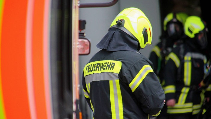 Symbolbild: Drei Feuerwehrleute vor einem Einsatzfahrzeug