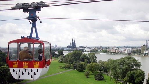 Blick auf Köln über die Pollerwiesen mit der Seilbahn und dem Kölner Stadtwappen.
