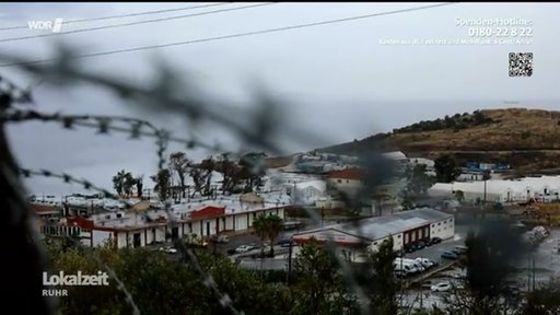 Ein Stacheldraht, dahinter das Flüchtlingscamp auf Lesbos