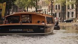 Das Bild zeigt die Grachten von Amsterdam im Vordergrund ein Boot.