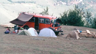 Ein alter Campingbus mit mehreren Zelten auf einer trockenen Wiese