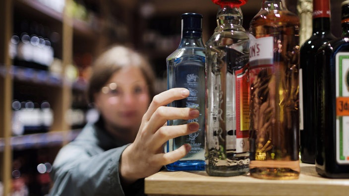 Eine junge Frau greift nach einer Flasche Alkohol