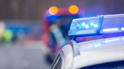 Nahaufnahme eines Polizeiwagens mit Blaulicht, im Hintergrund ist ein Feuerwehrwagen zu sehen.