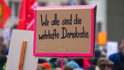 Ein Plakat ·Wir alle sind die wehrhafte Demokratie· wird auf einer Kundgebung gegen Rechtsextremismus gezeigt